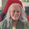Grey-haired woman smiling in green jacket.
